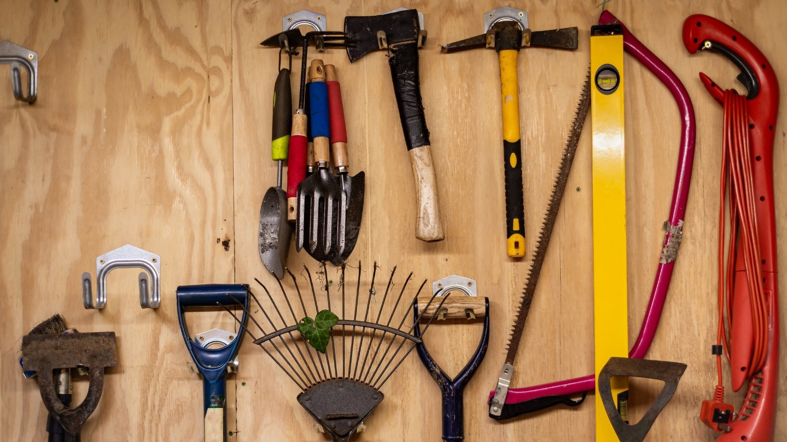 A neatly arranged assortment of small digging, cutting, and raking equipment, organized against a wooden board.